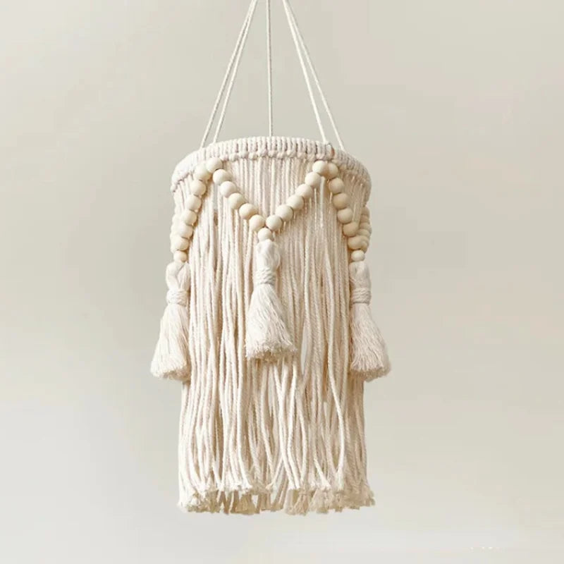  abat-jour nordique en macramé avec des perles et des franges décoratives suspendu au plafond, éclairé.