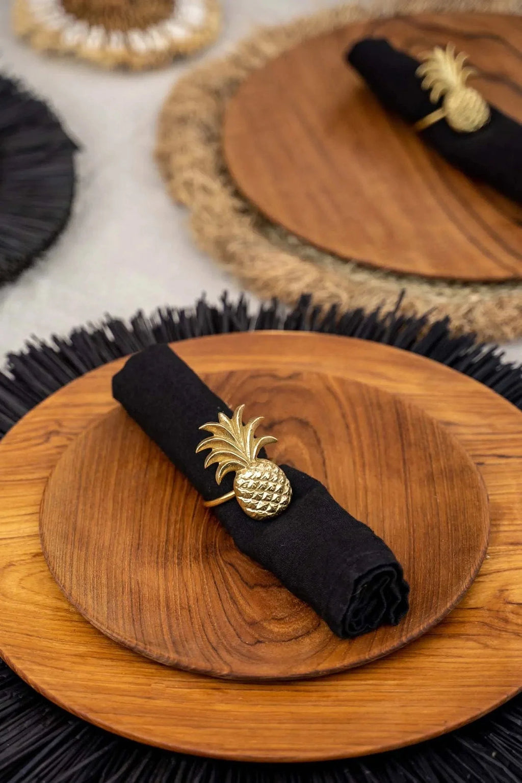 Serviette noire avec anneau en or en forme d’ananas sur une assiette en teck naturel