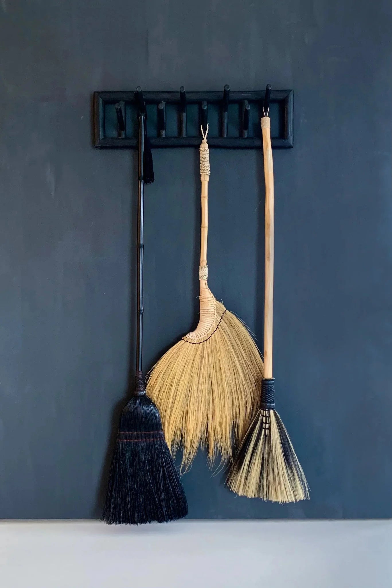 Balai décoratif en fibres noires avec poignée bambou et détails tressés suspendus