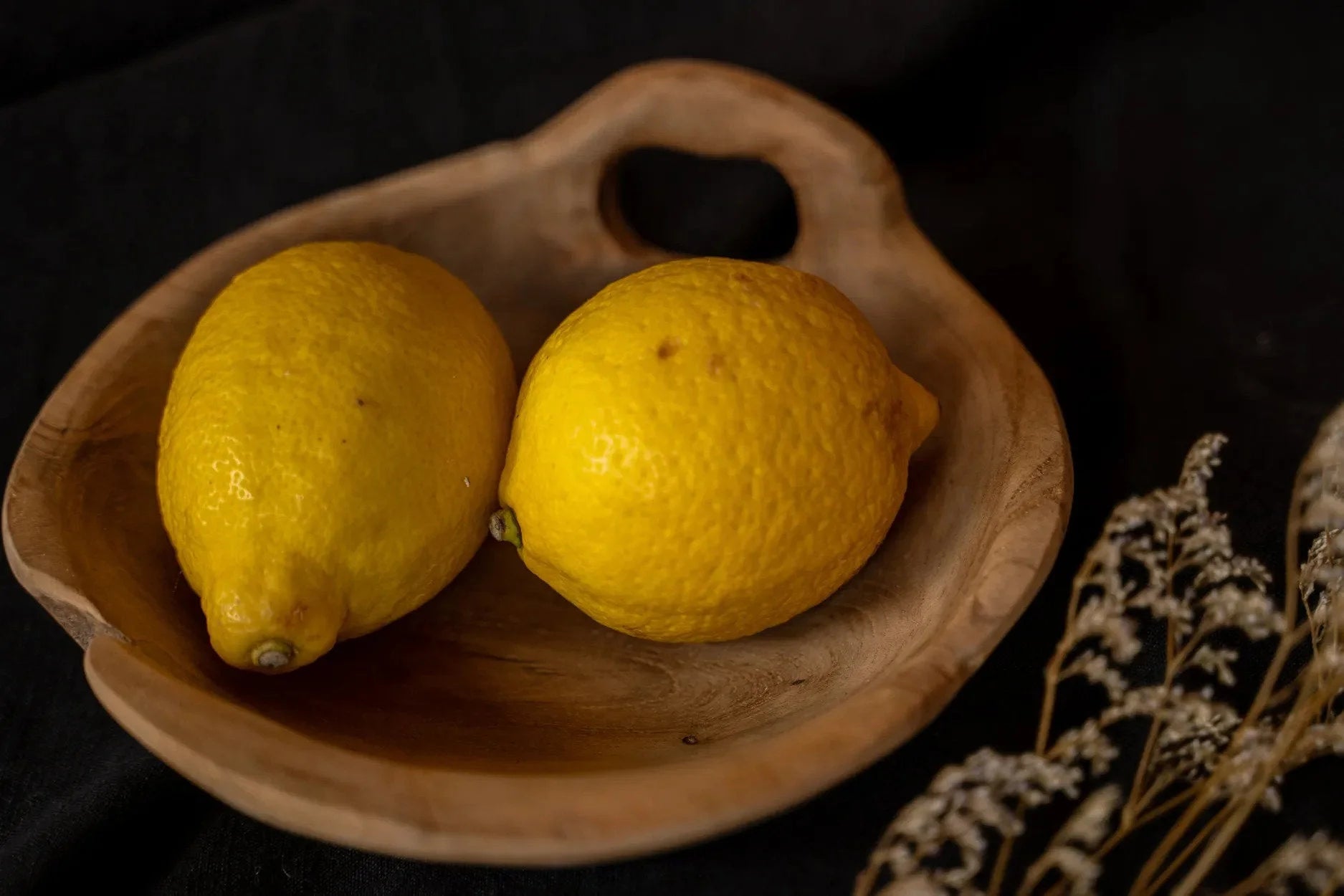 Deux citrons jaunes mûrs dans un bol en bois de teck avec poignée intégrée naturelle