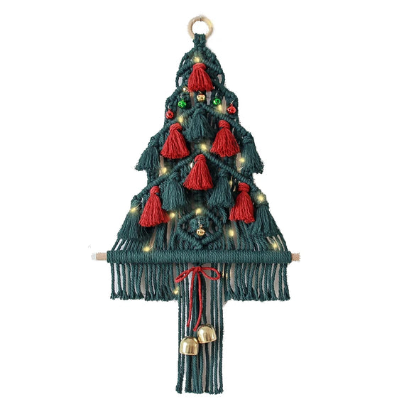 Décoration murale sapin de Noël en macramé sur fond blanc, avec pompons rouges et clochettes dorées.