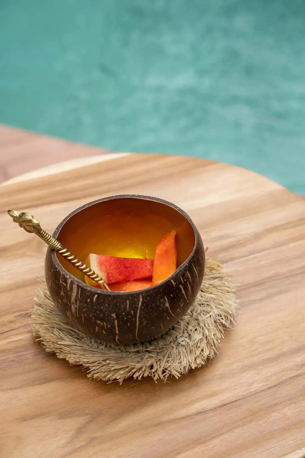 Verre en coque de noix de coco brun avec tranches d’orange et paille sur sous-verre rond en raphia naturel à franges solaires