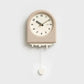 Horloge à pendule moderne beige avec un effet fonte suspendue sur un mur blanc dans un intérieur épuré.