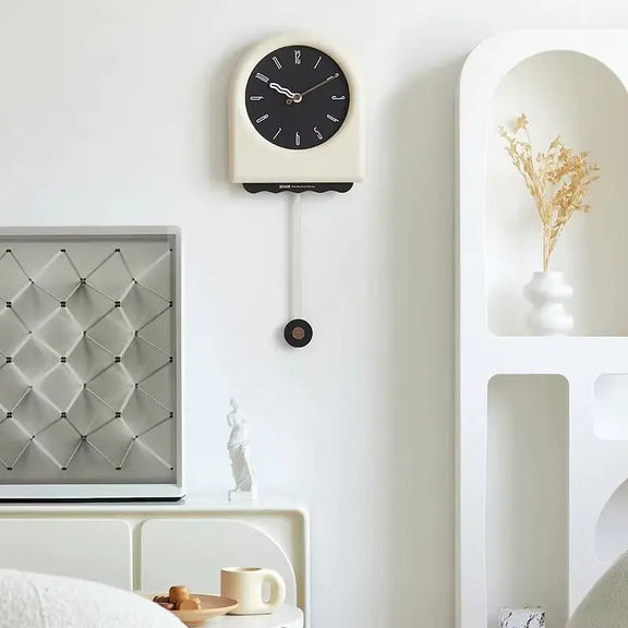 Horloge à pendule moderne crème avec cadran noir installée sur un mur blanc dans un intérieur design et épuré.