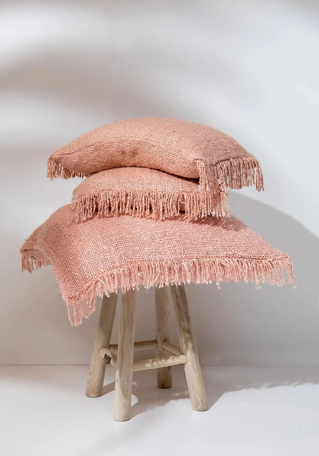 Coussin rectangulaire rose saumon avec franges, textured, sur un tabouret en bois clair