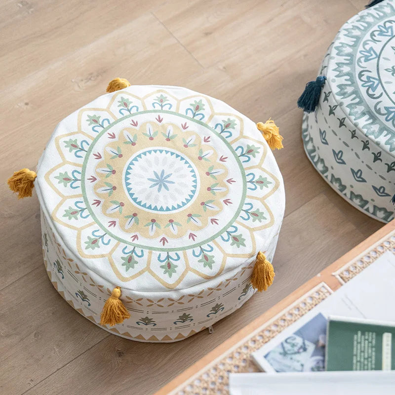 Housse de pouf rond avec motif jaune et pompons, posée sur un sol en bois dans un salon bohème.