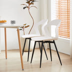 Deux chaises contemporaines blanches avec pieds en métal noir placées près d’une table dans une pièce lumineuse.