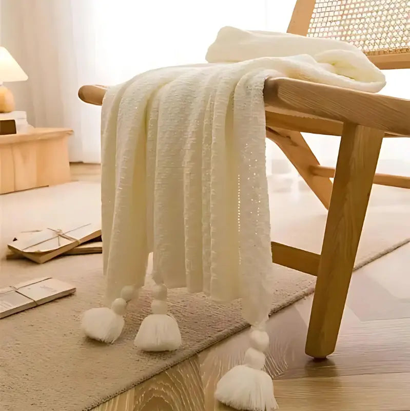 Plaid blanc en maille gaufrée avec pompons sur une chaise en bois