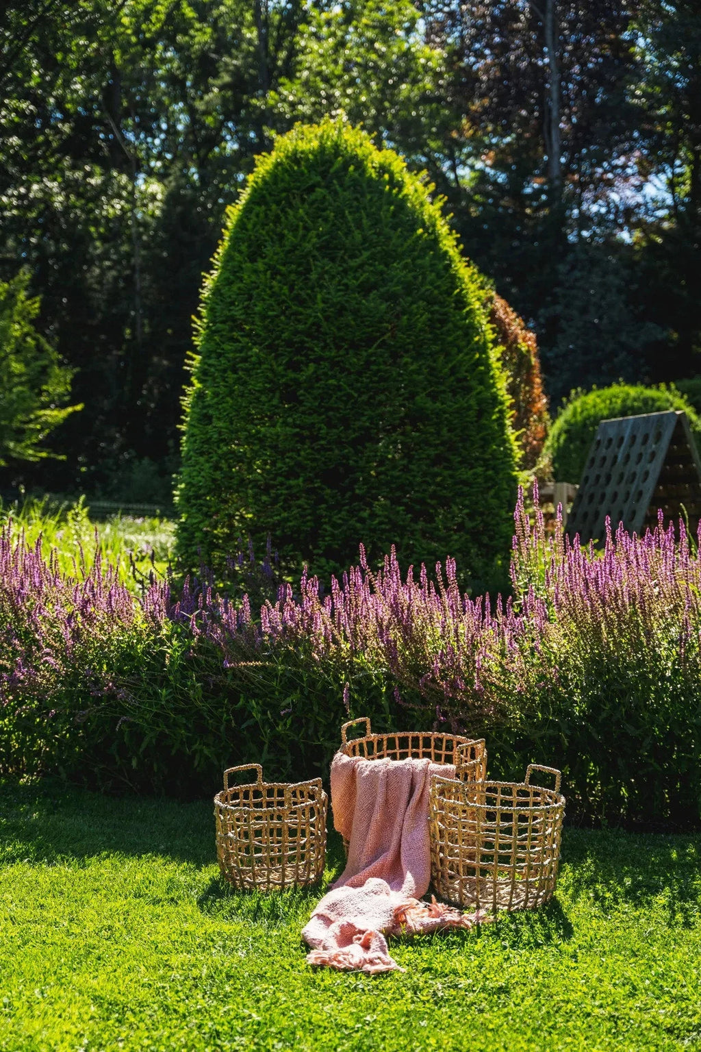 Trois paniers en rotin avec une couverture rose saumon dans un jardin coloré
