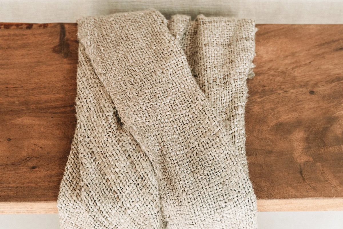 Tissu tissé beige à franges, plié sur une surface en bois, pour décoration lit ou canapé
