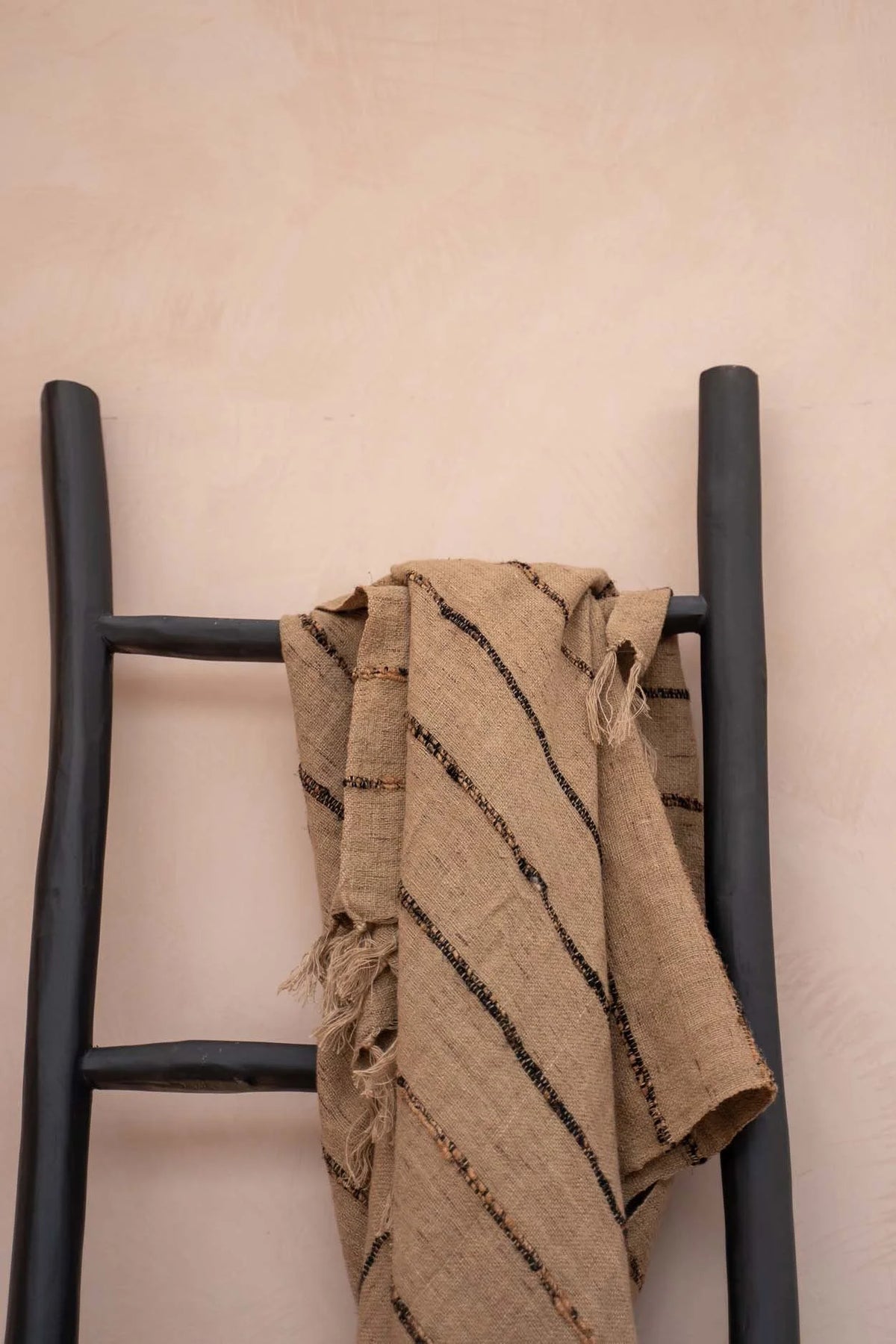 Plaid en coton tissé beige rayé avec franges, drapé sur une échelle noire
