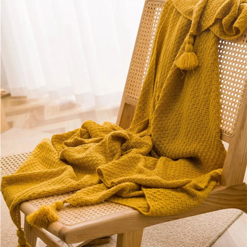 Plaid moutarde en maille gaufrée avec pompons, drapé sur une chaise en bois