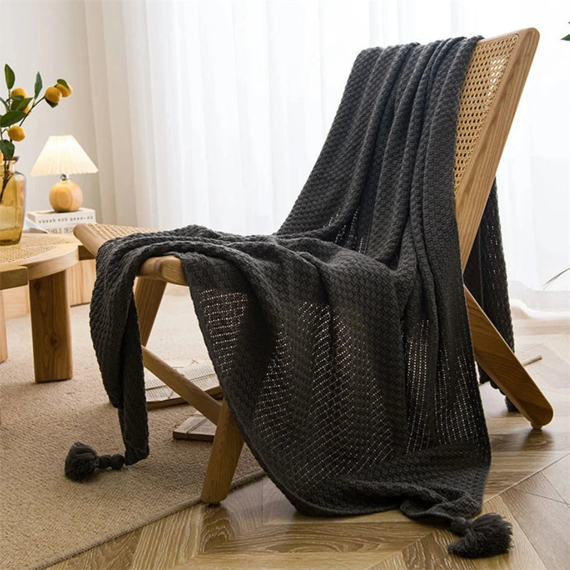 Plaid noir en maille gaufrée posé sur une chaise en bois avec pompons