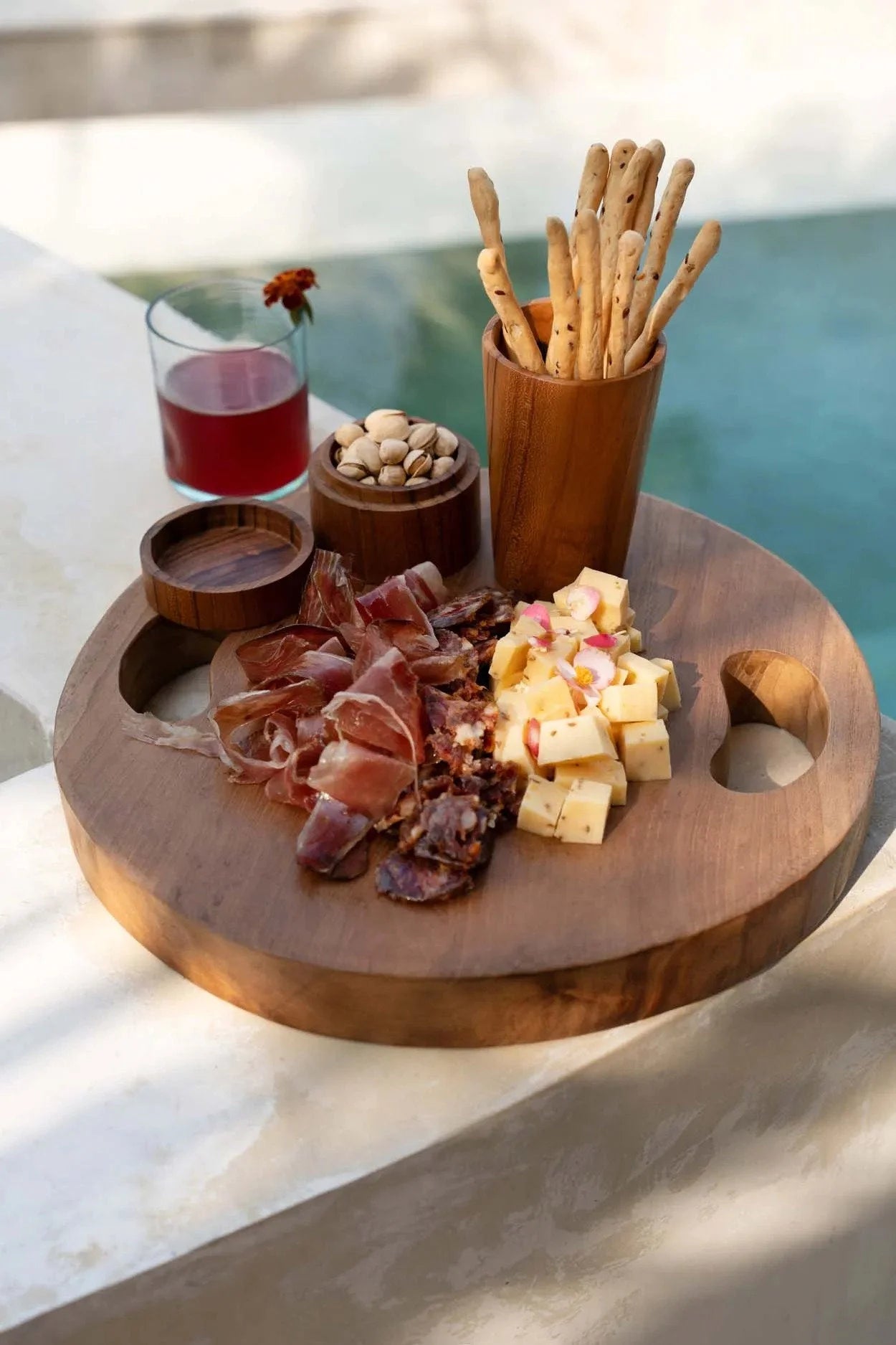 Plateau rond en racine de teck avec poignées en bois clair, assortiment de charcuterie et fromages