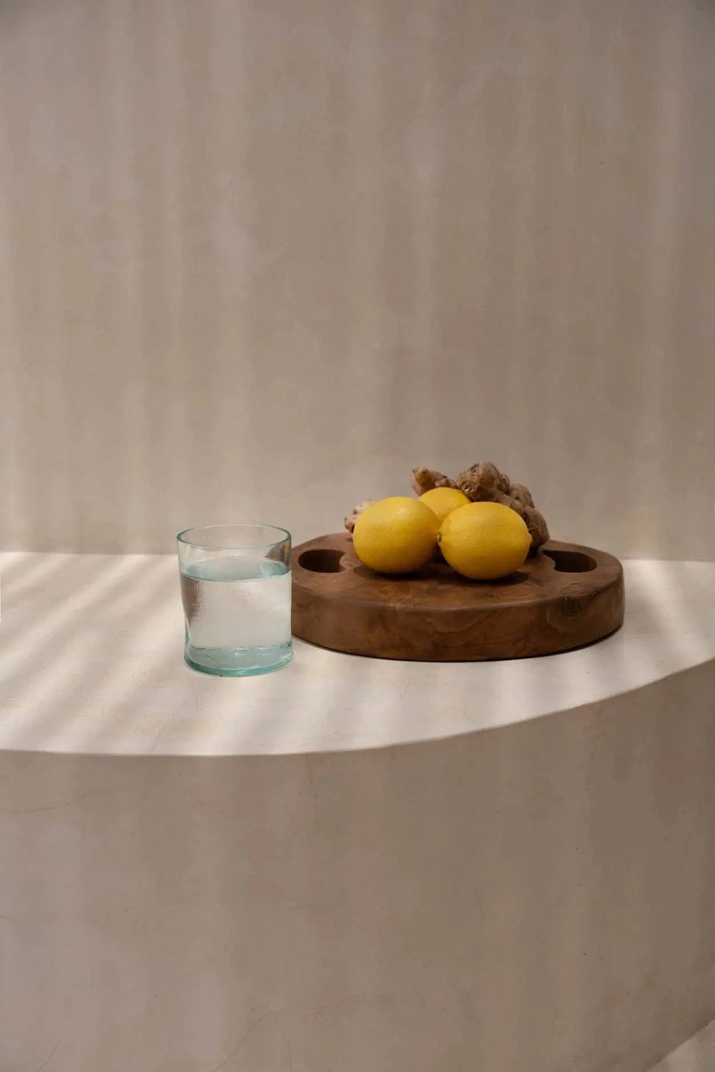 Plateau rond en teck naturel avec poignées ajourées, contenant trois citrons et gingembre