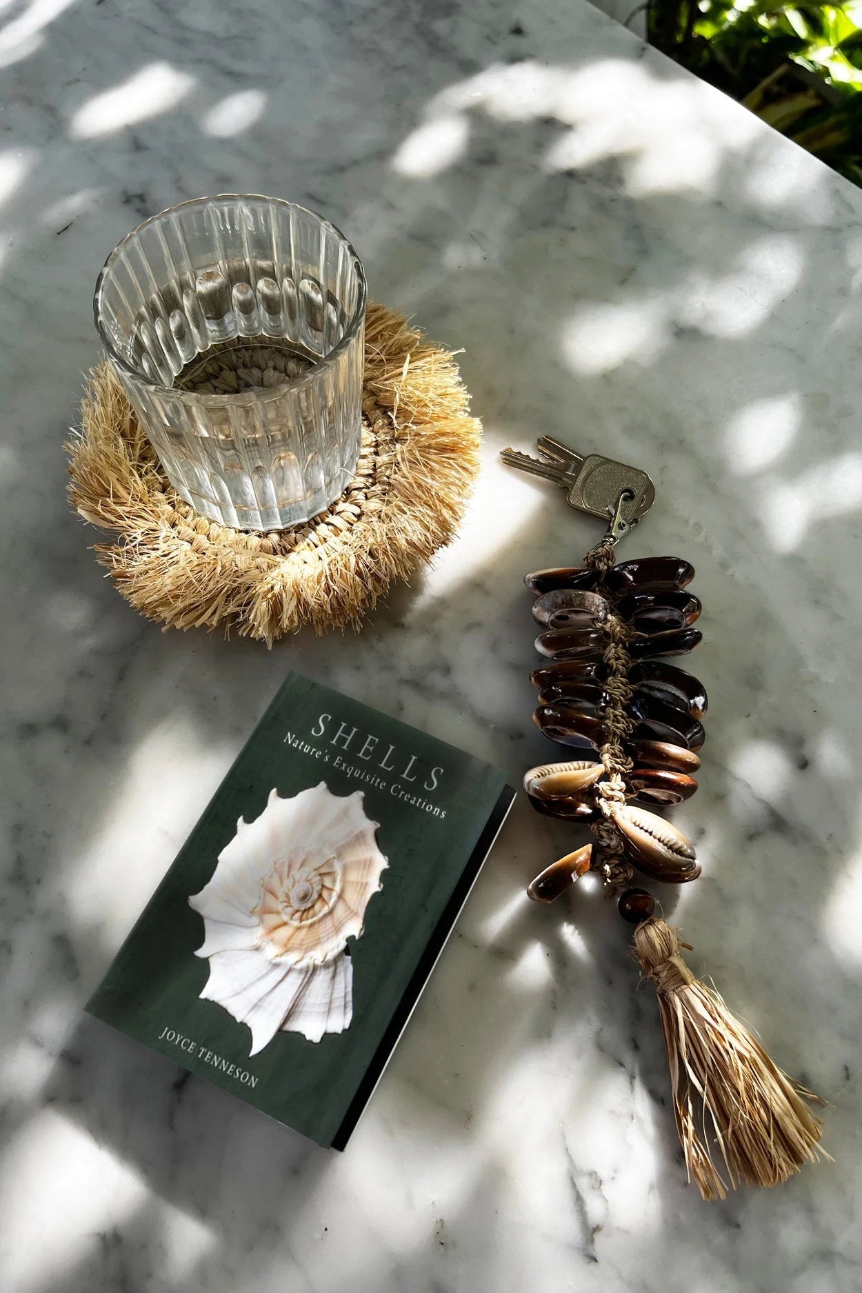Livre vert foncé avec coquillage blanc sur la couverture, porte-clés en coquillages et raphia