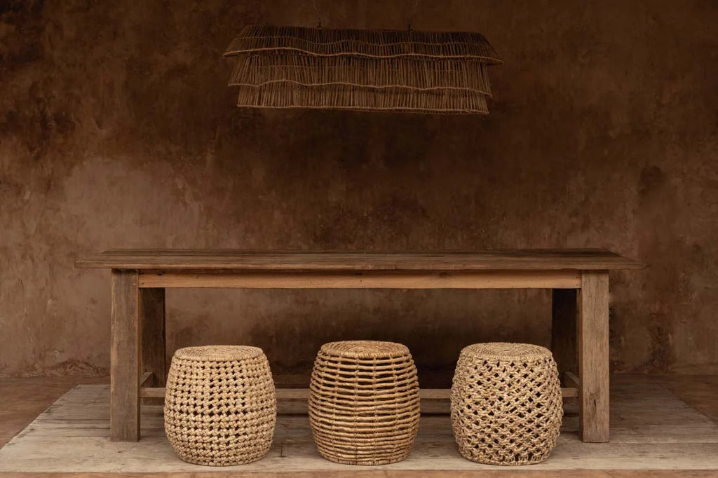 Trois tabourets en rotin tissé beige naturel devant table rustique en bois