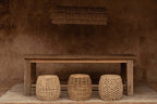 Trois tabourets en rotin tissé beige naturel devant table rustique en bois