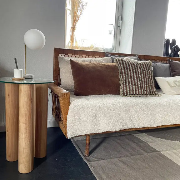 Petite table basse ronde en verre et bois mise en situation dans un salon lumineux avec un canapé et des coussins chaleureux.