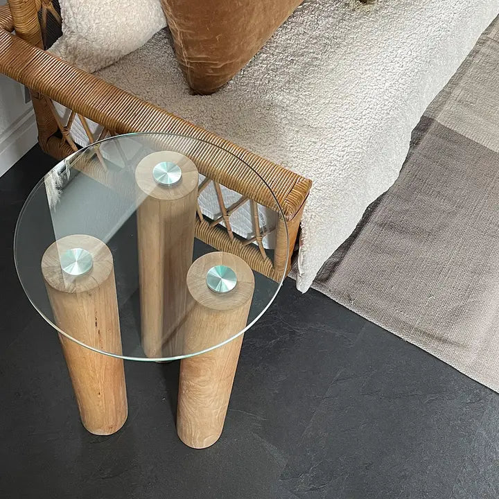 Vue de dessus de la petite table basse ronde en verre et bois, placée à côté d’un canapé en rotin.

