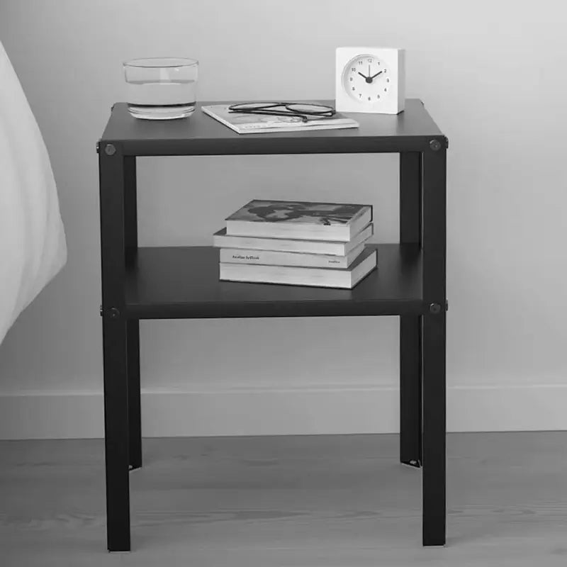 Table de chevet en métal noir décorée avec des livres, un verre et des objets design.