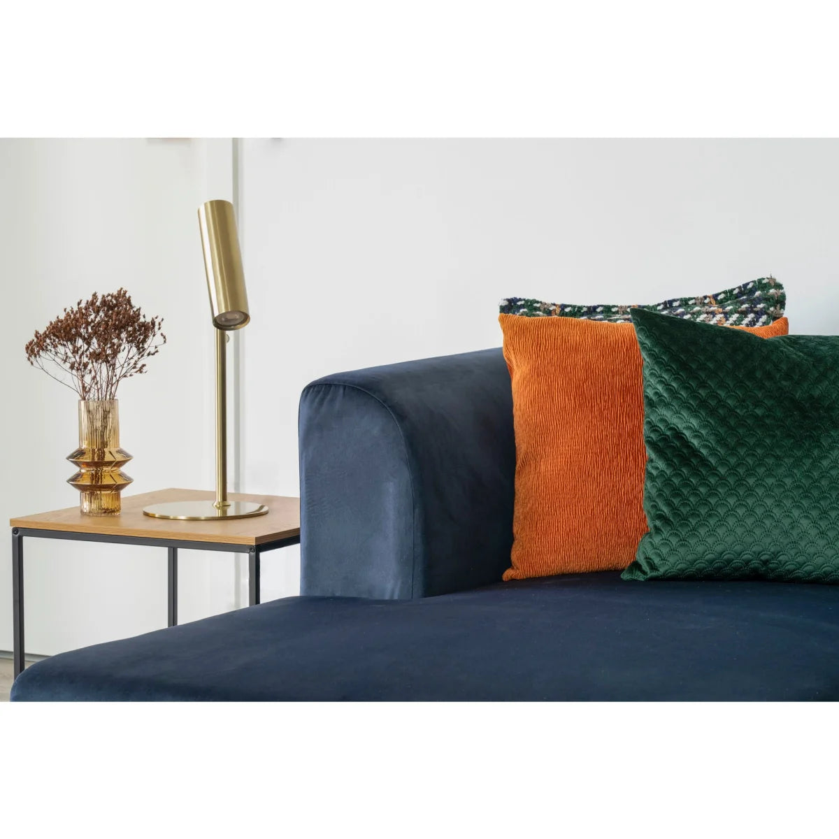 Canapé en velours bleu marine avec coussins orange et vert texturés