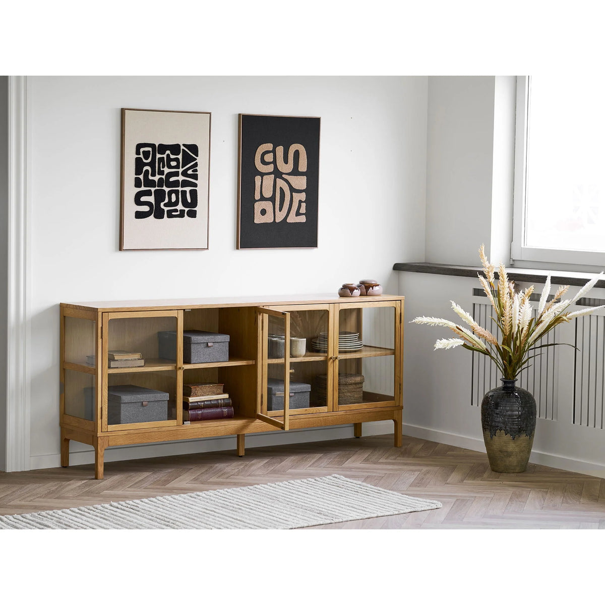 Buffet en bois clair avec portes vitrées et étagères ouvertes, affichant boîtes et objets décoratifs