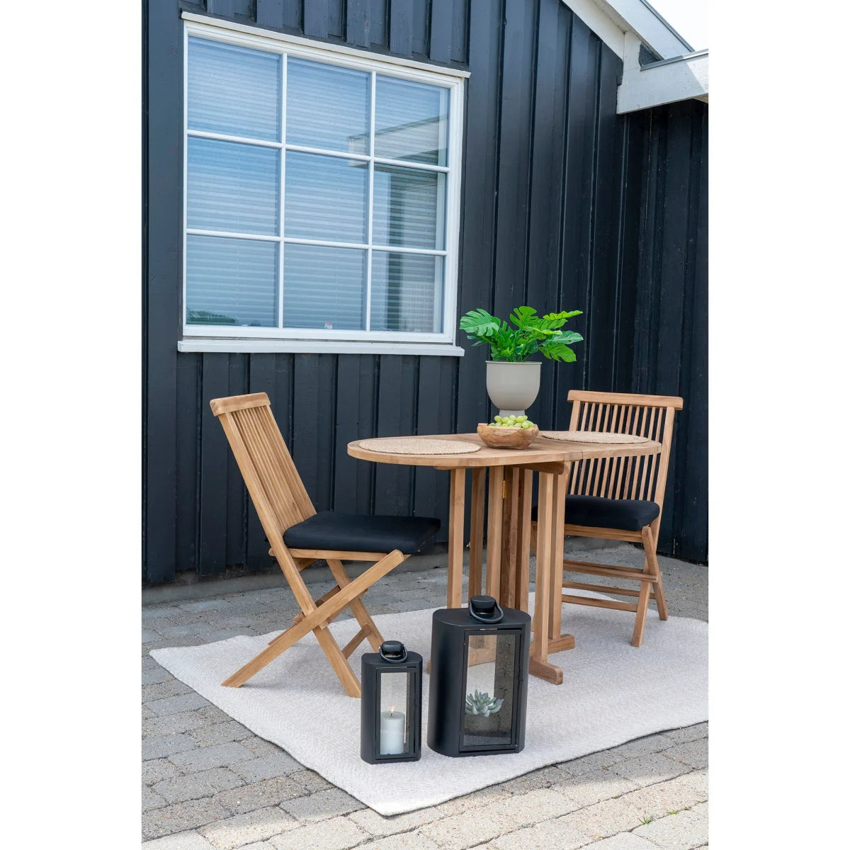 Table ovale en teck avec chaises pliantes rembourrées noires et lanternes noires
