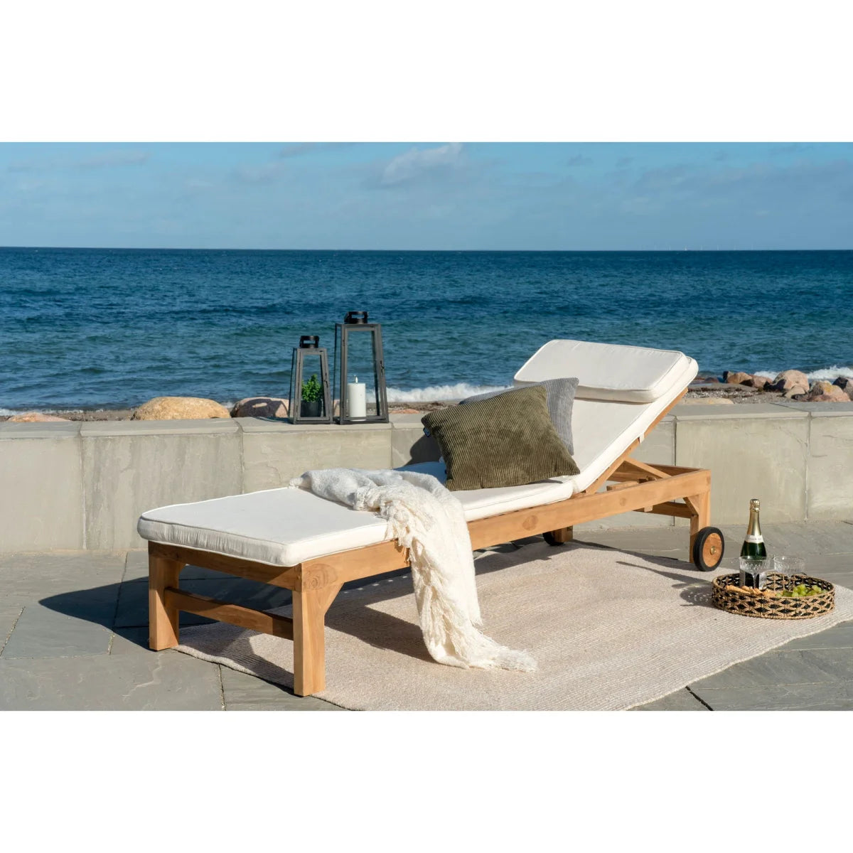 Chaise longue en teck clair avec coussin blanc, oreiller vert olive et plaid crème sur tapis chevron sable recyclé 140x200 cm