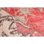 Tapis vintage rouge et beige à motifs, partiellement roulé pour révéler le dessous