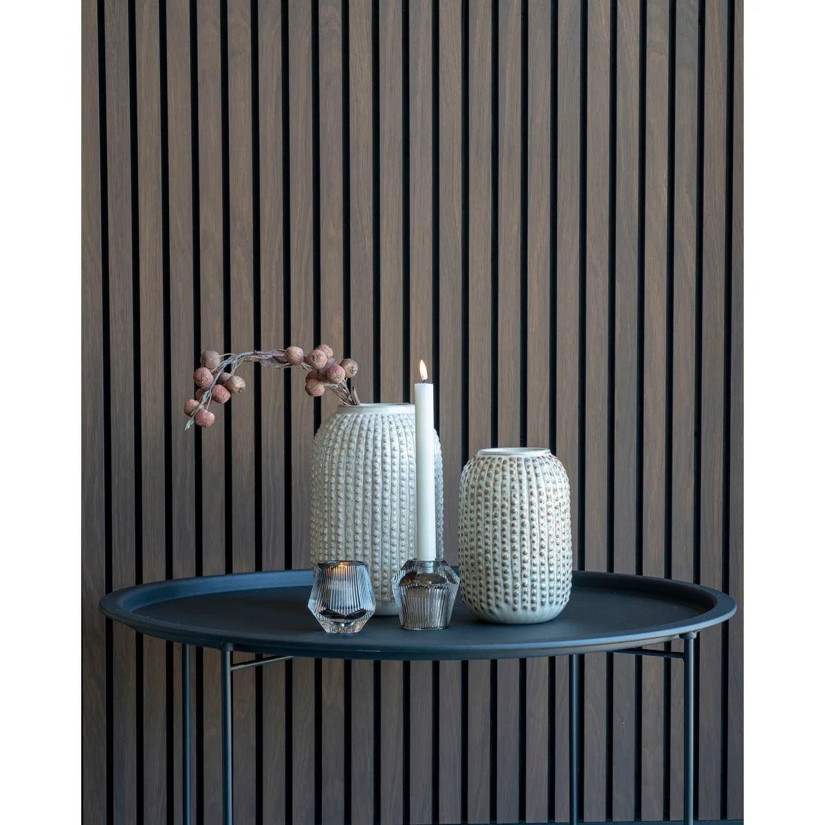 Deux vases céramique texturés écru à col étroit, l’un avec baies séchées, l’autre près d’une bougie allumée sur table sombre