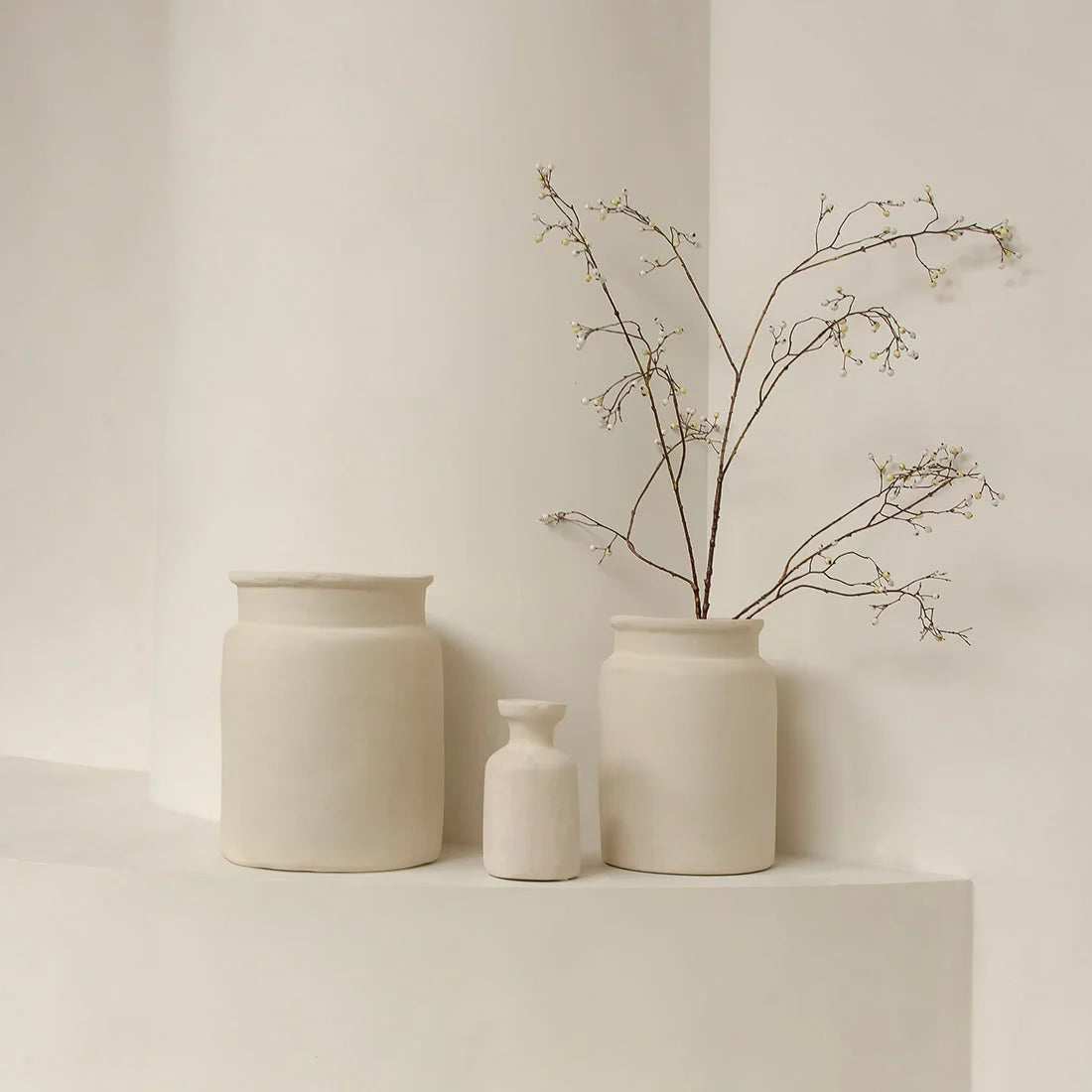 Trois vases céramiques beige minimalistes, un avec branches séchées