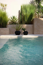Vase en terre cuite et raphia noir naturel H19 cm devant une piscine turquoise avec plantes en pot